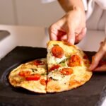 Close-up of hands serving a delicious Margherita pizza slice indoors.