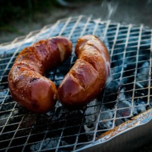 Close-up of grilled sausages on a barbecue grill with smoke rising.