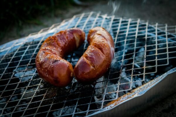 Close-up of grilled sausages on a barbecue grill with smoke rising.