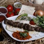 Delicious grilled shish kebab served with fresh vegetables, herbs, and spices on a plate.