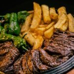 Sizzling grilled beef served with crispy french fries and green peppers on a hot plate.