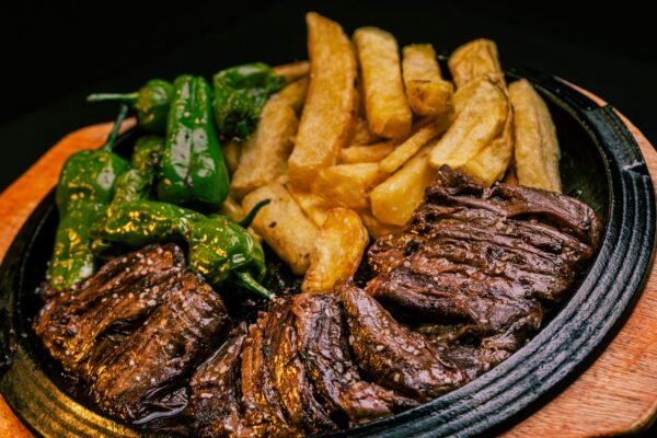 Sizzling grilled beef served with crispy french fries and green peppers on a hot plate.