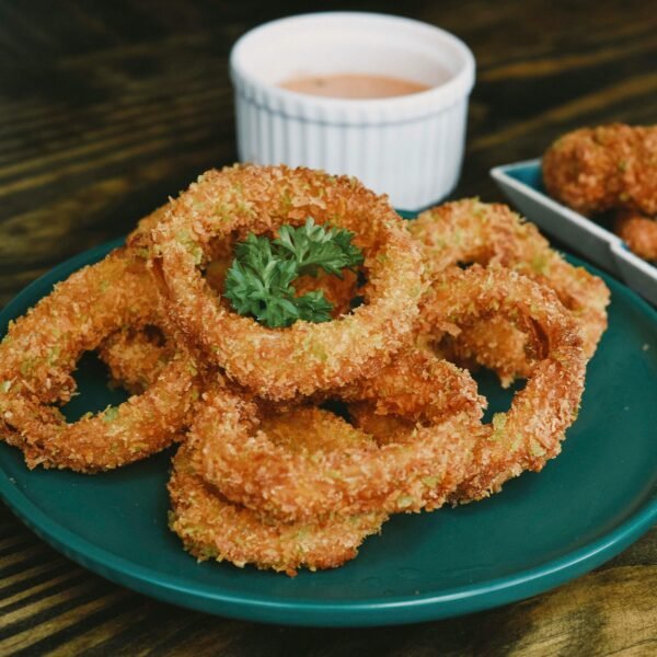 Golden brown onion rings served on a teal plate with a side of dipping sauce.