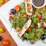 Top view of a Mediterranean salad with halloumi, olives, and cherry tomatoes.