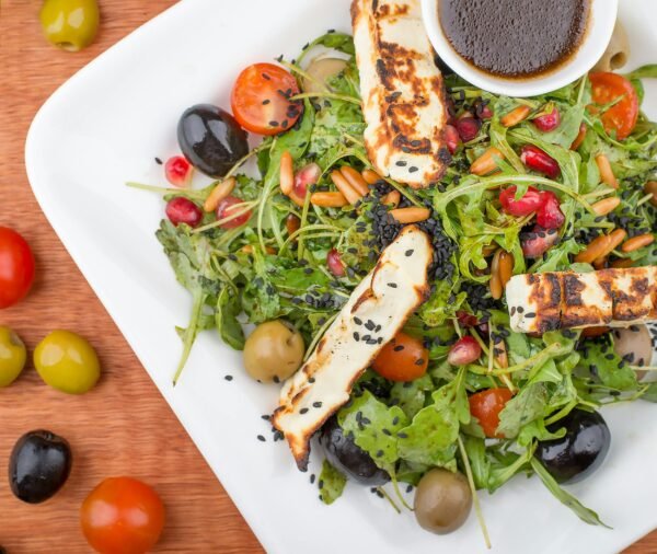 Top view of a Mediterranean salad with halloumi, olives, and cherry tomatoes.