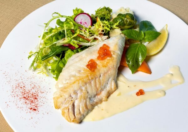 Delicious grilled fish fillet served with fresh mixed greens and sauce on a plate.