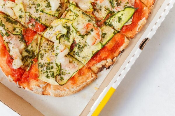 Delicious Italian pizza topped with zucchini and shrimp, captured from above in a cardboard box.