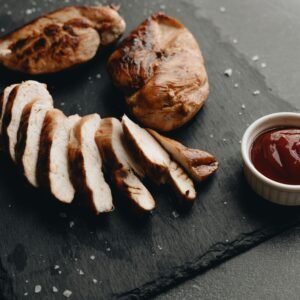 Sliced grilled chicken breast with dipping sauce on a slate surface.