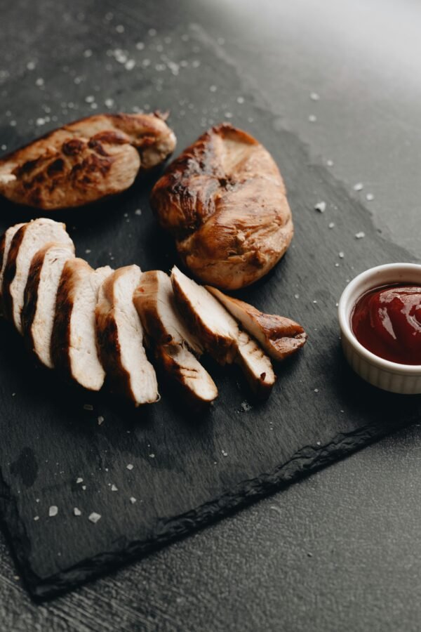 Sliced grilled chicken breast with dipping sauce on a slate surface.