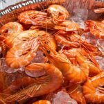 A vibrant display of fresh orange shrimps on a bed of crushed ice, perfect for a seafood feast.