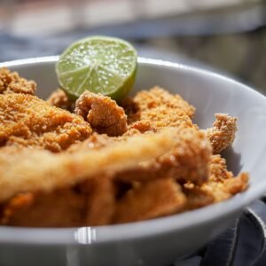 Close-up of crispy fried chicken strips in a white bowl with a lime wedge.