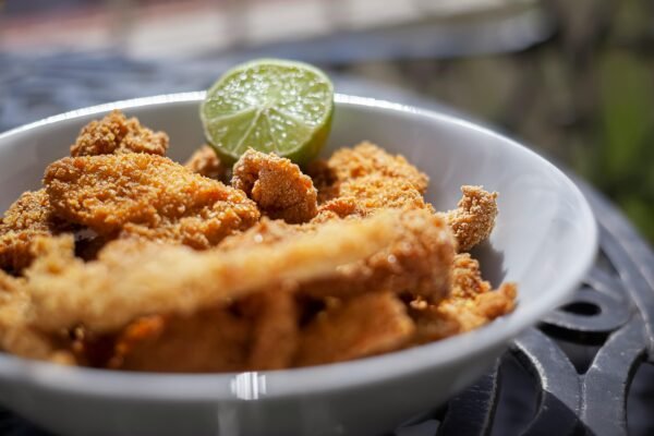 Close-up of crispy fried chicken strips in a white bowl with a lime wedge.