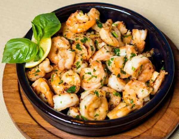 Delicious grilled shrimp with herbs and lemon in a wooden bowl.