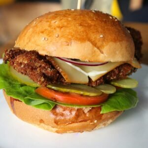 Delicious crispy chicken burger with fresh veggies and cheese on a sesame seed bun, served on a plate.