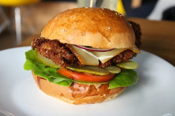 Delicious crispy chicken burger with fresh veggies and cheese on a sesame seed bun, served on a plate.